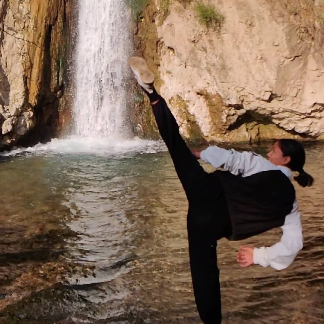 A student holding a high side kick mid-air against a waterfall.